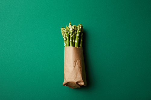 top view of bunch of ripe asparagus covered with kraft paper on green surface