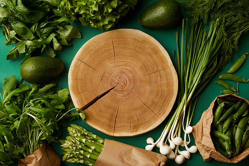 top view of wood cut surrounded with various ripe vegetables on green surface