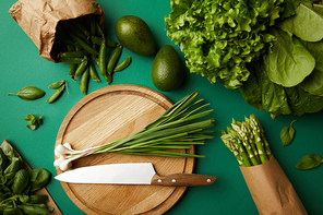 top view of different ripe vegetables with wooden cutting board and knife on green surface