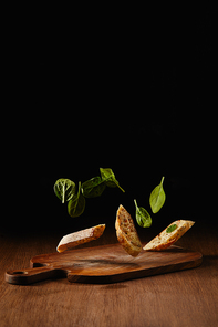 Bread pieces and salad leaves flying above wooden cutting board