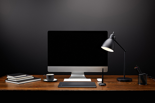 close up view of graphic designer workplace with graphic tablet, blank computer screen, notebooks and cup of coffee on wooden tabletop