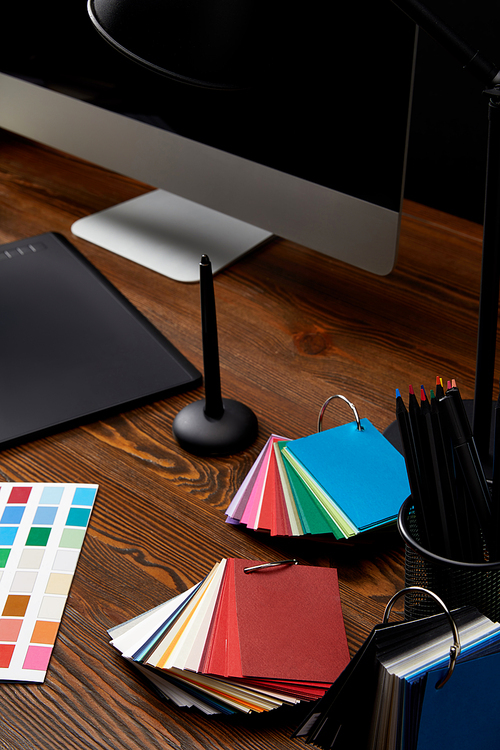 close up view of graphic designer workplace with colorful pallet, graphic tablet and computer screen on wooden surface