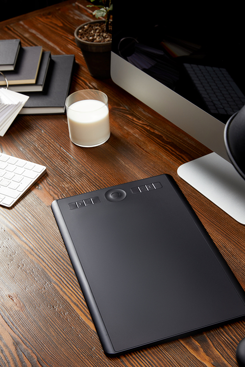 close up view of graphic designer workplace with graphic tablet, glass of milk and notebooks on wooden tabletop