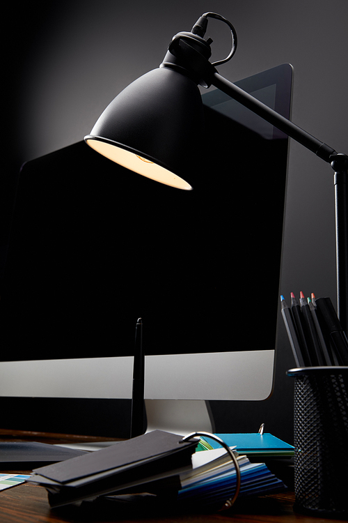 close up view of designer workplace with lamp and blank computer screen on wooden tabletop