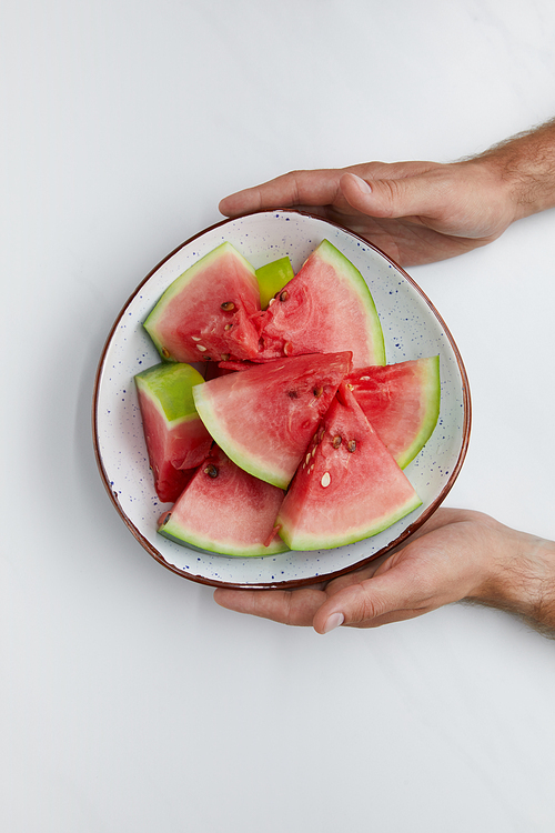 partial view of man holding bowl with watermelon pieces in hands on white surface