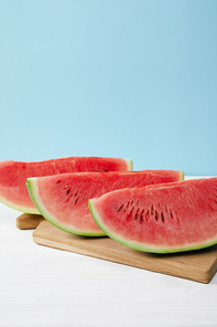 close up view of arranged watermelon slices on cutting board on white surface on blue backdrop