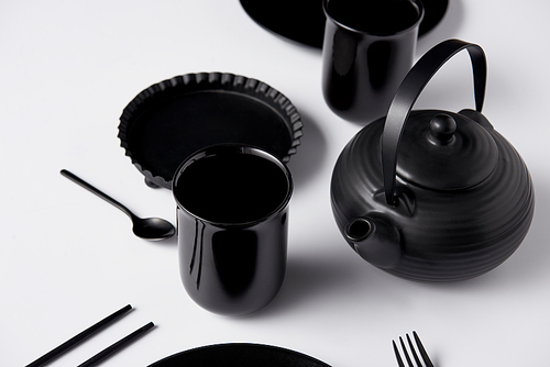 selective focus of black teapot, cups, fork, spoon, chopsticks and baking dish on white table