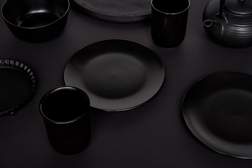 selective focus of black teapot, bowl, baking dish, cups and plates on black table