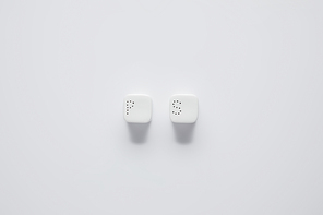 top view of pepper caster and saltcellar on white table, minimalistic concept