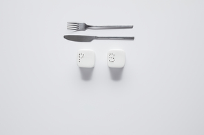 top view of fork, knife, saltcellar and pepper caster on white table, minimalistic concept