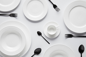 top view of various plates, cup, black spoons and forks on white table