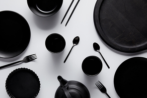 top view of black teapot, spoons, forks, chopsticks, cups, tray, bowl, plates and baking dish on white table