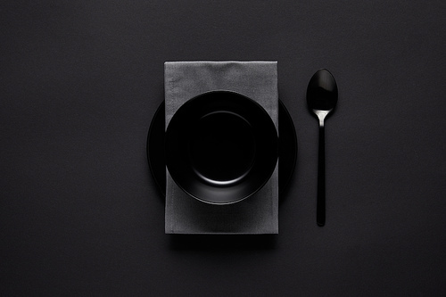 top view of black bowl, spoon, kitchen towel and plate on black table, minimalistic concept