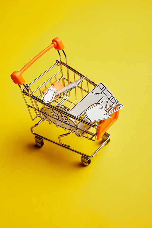 close up view of little shopping cart with clothes made of paper on yellow background
