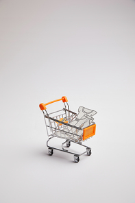 close up view of shopping cart with little goods made of paper on grey background