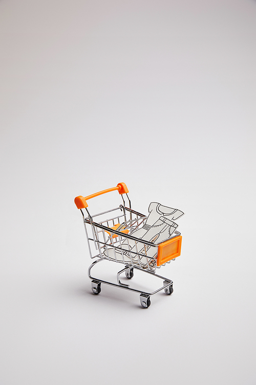 close up view of shopping cart with little goods made of paper on grey background