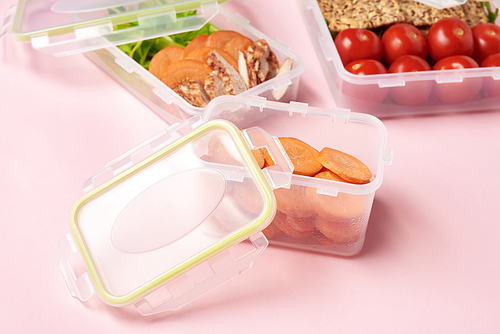 close up view of healthy food arranged in food containers on pink backdrop