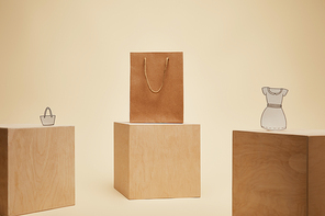 paper shopping bag, paper bag and paper dress on wooden cubes isolated on beige