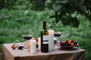 candles, wine and fruits on table in garden for dinner