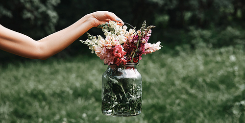 partial view of woman holding glass jar with various colorful flowers