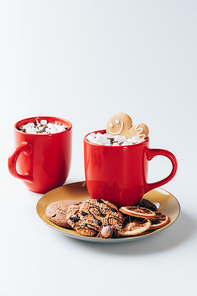 plate with cookies and cups of hot cacao with marshmallows, on white
