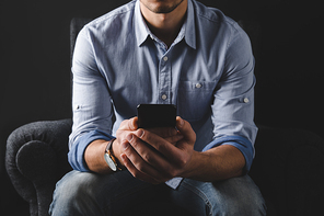 cropped view of man using smartphone while sitting in armchair