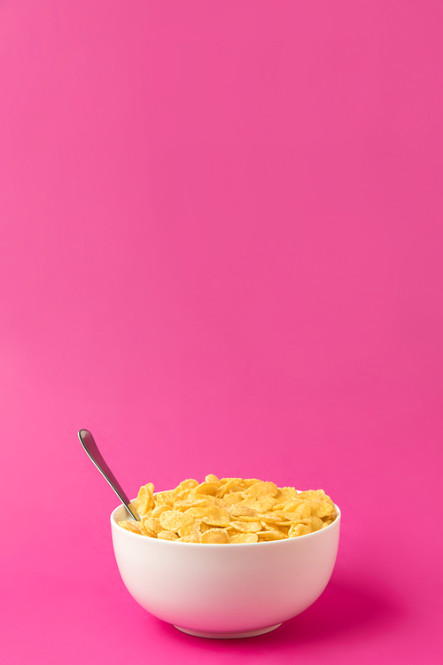 healthy breakfast with tasty corn flakes and milk in bowl with spoon isolated on pink