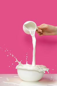 cropped shot of person pouring fresh healthy milk from jug to bowl on pink