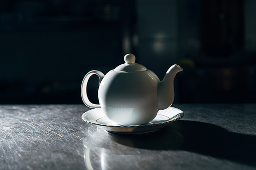 vintage teapot on plate on metal surface in dark room