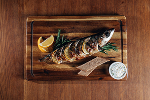 top view of grilled fish with lemon and rye bread on wooden board
