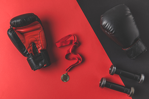 top view of boxing gloves with medal and dumbbells on red and black surface