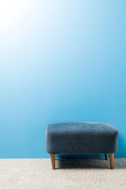 soft hassock standing on carpet in front of blue wall
