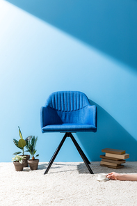 comfy blue armchair with person holding cup of coffee on floor in front of blue wall