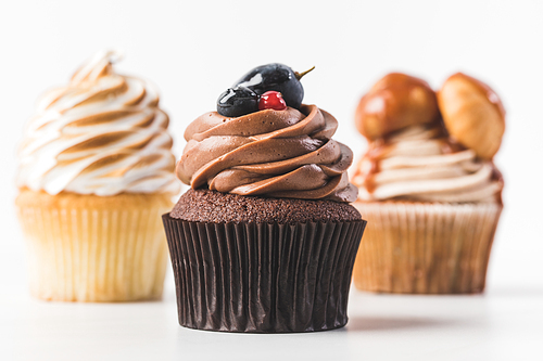 close up view of chocolate cupcake with cream, berries and plum isolated on white