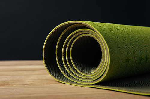 green rolled yoga mat on wooden tabletop on black