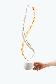partial view of hand holding white cup with splashes of milk and aromatic coffee, isolated on white