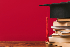 Cropped view of stack of books with academic cap on red