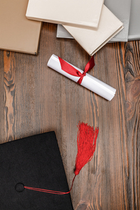 Top view of books, diploma and academic cap on wood background