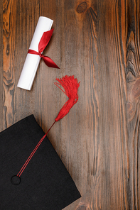 Top view of diploma and square academic hat on wood background