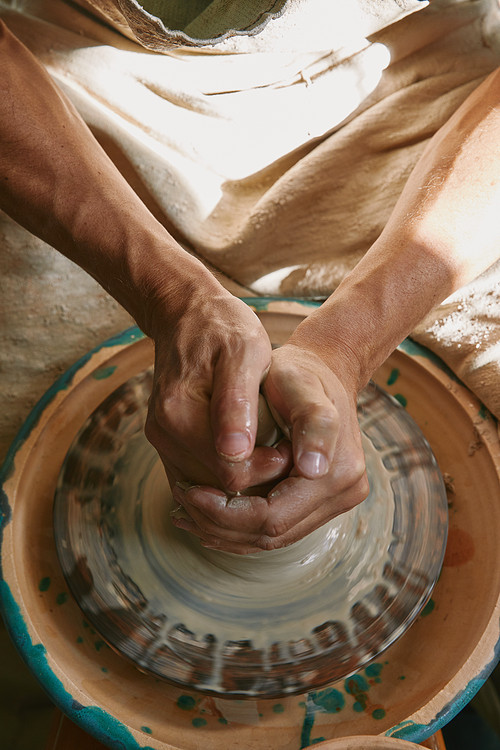 partial view of professional potter working on pottery wheel at workshop