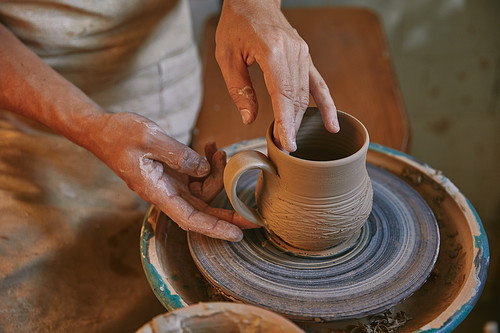 cropped image of professional potter working on pottery wheel at workshop