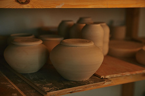 close up view of ceramic bowls and dishes on wooden shelves at pottery studio