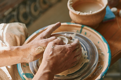 close up view of man hands working on pottery wheel at workshop