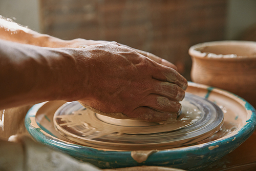 selective focus of male potter hands working on pottery wheel at workshop