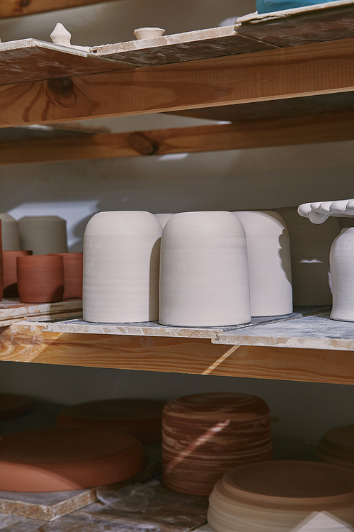 selective focus of ceramic bowls and dishes on wooden shelves at pottery studio