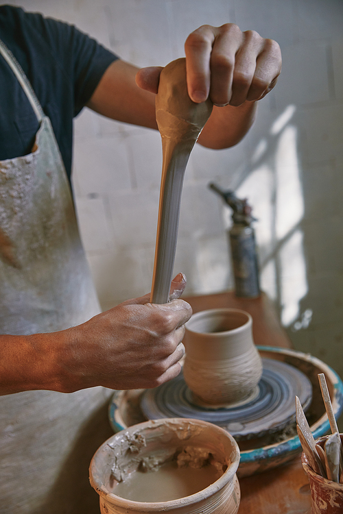 cropped image of professional potter in apron working with clay at pottery studio