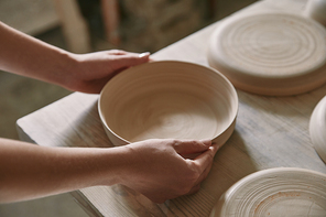 partial view of woman putting ceramic dish on table at workshop