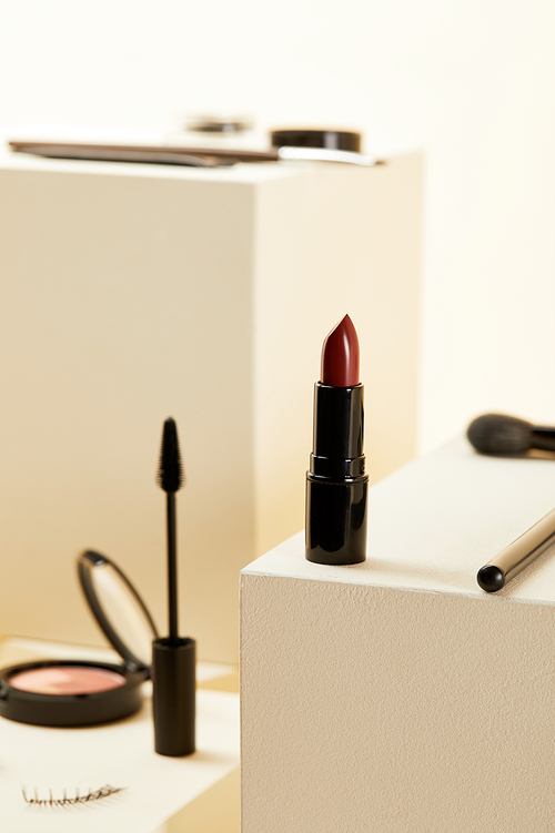 close-up shot of red lipstick with various makeup accessories on beige cubes