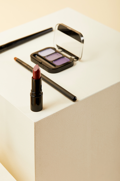 close-up shot of lipstick with purple eyeshadows case and brushes on beige