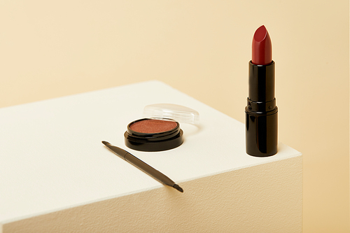 close-up shot of lipstick standing on beige surface with can of blush and brush